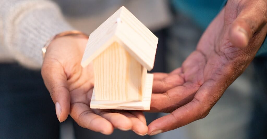 Close-up of hands holding a small wooden house, representing real estate and new home ownership.